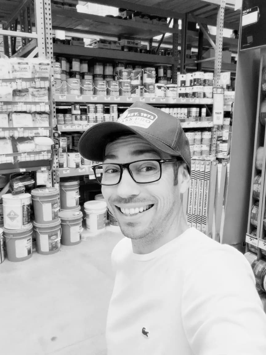 Shawn Nicholson smiling, wearing glasses and a cap, in a hardware store.